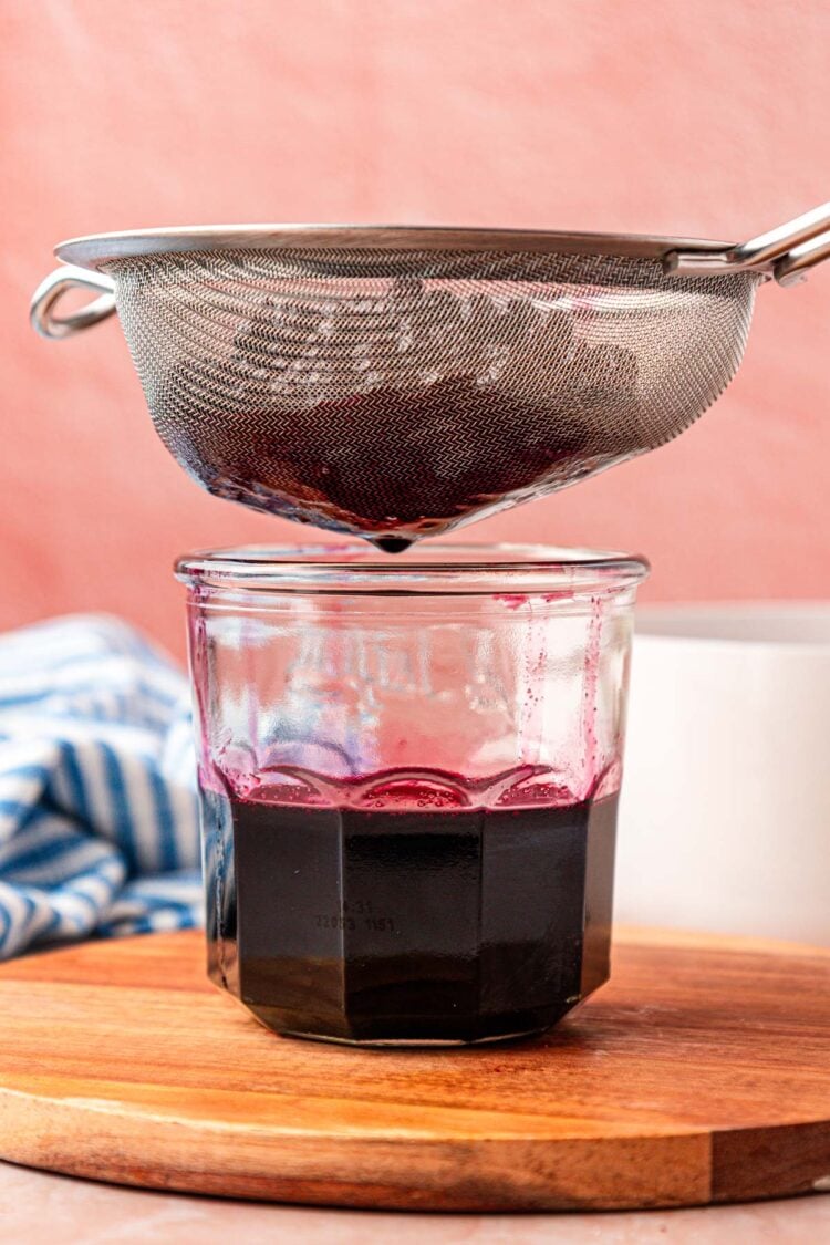 A fine mesh sieve straining blueberry simple syrup.