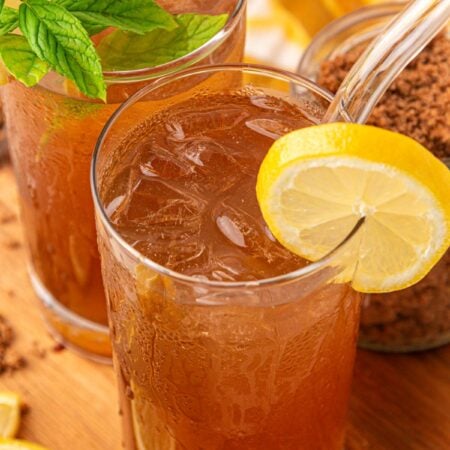 Two glasses of brown sugar lemonade on a wooden board with a pitcher behind it.