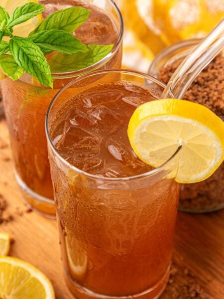 Two glasses of brown sugar lemonade on a wooden board with a pitcher behind it.