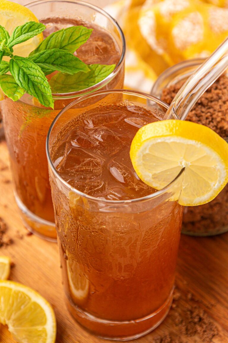 Two glasses of brown sugar lemonade on a wooden board with a pitcher behind it.