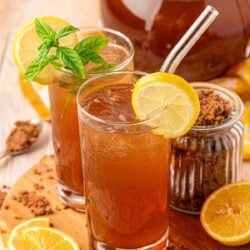 Two glasses of brown sugar lemonade on a wooden board with a pitcher behind it.