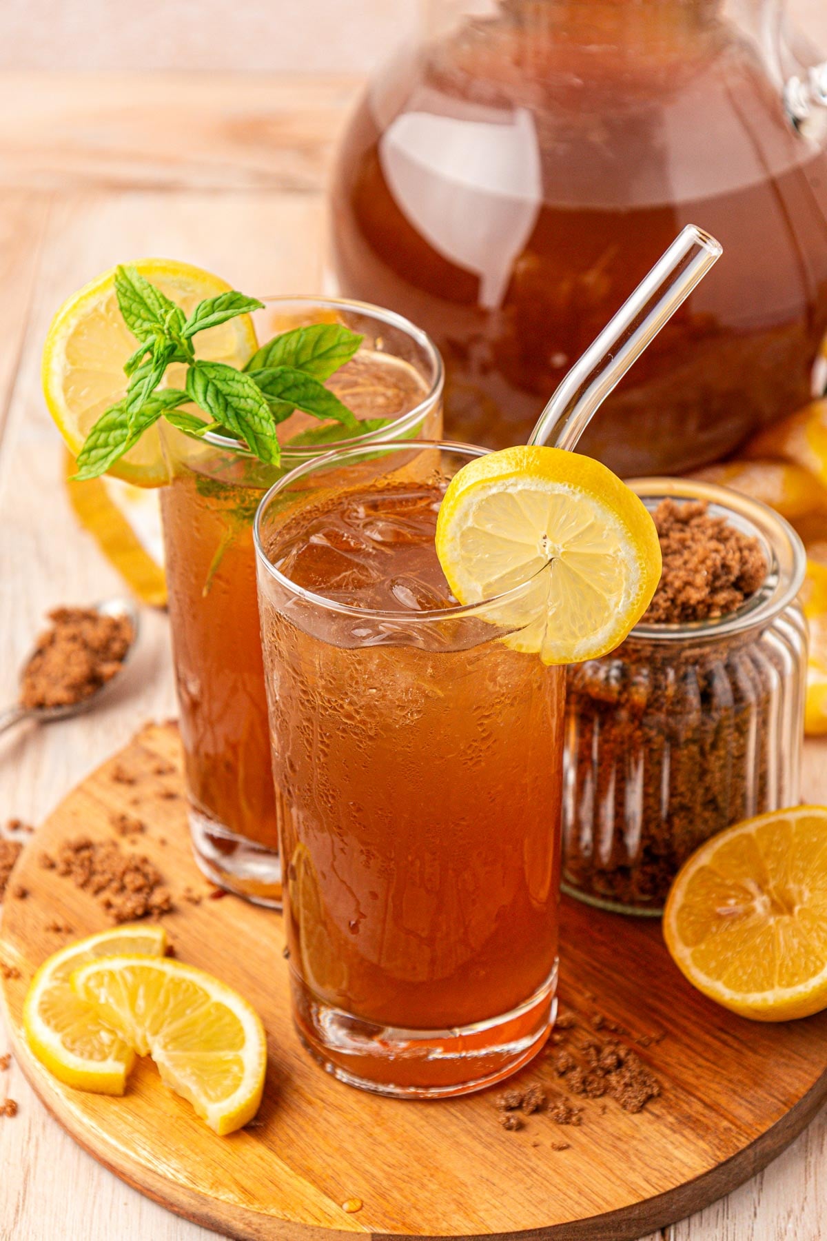 Two glasses of brown sugar lemonade on a wooden board with a pitcher behind it.