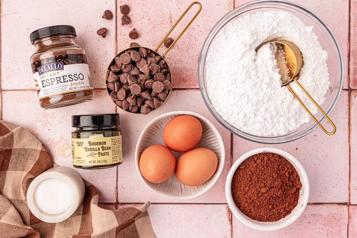 Ingredients to make flourless brownie cookies on a pink tile surface.