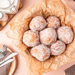 Overhead photo of Malasadas in a basket with parchment paper.