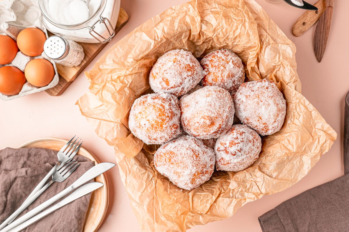 Overhead photo of Malasadas in a basket with parchment paper.