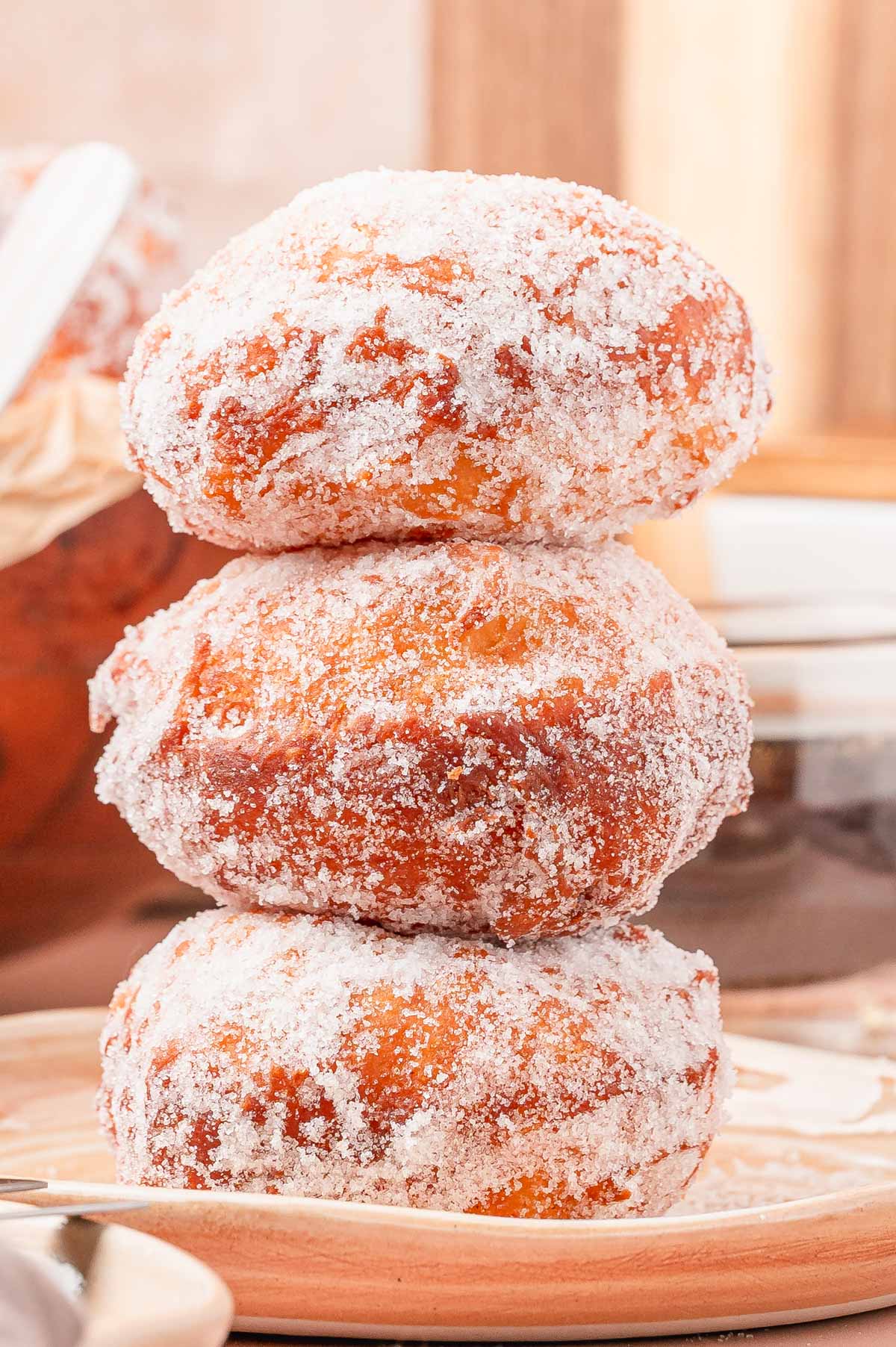 A stack of three malasadas on a tan plate.