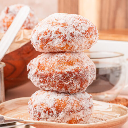 A stack of three malasadas on a tan plate.