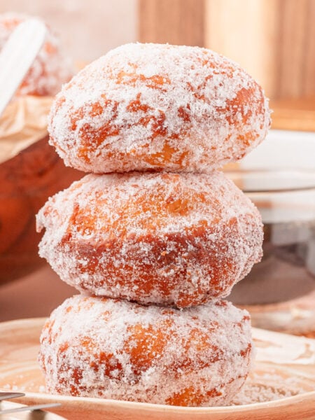 A stack of three malasadas on a tan plate.