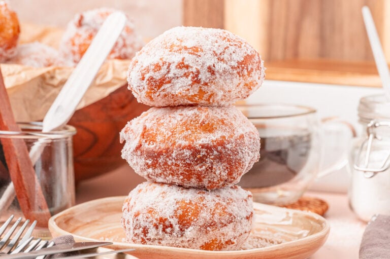 A stack of three malasadas on a tan plate.