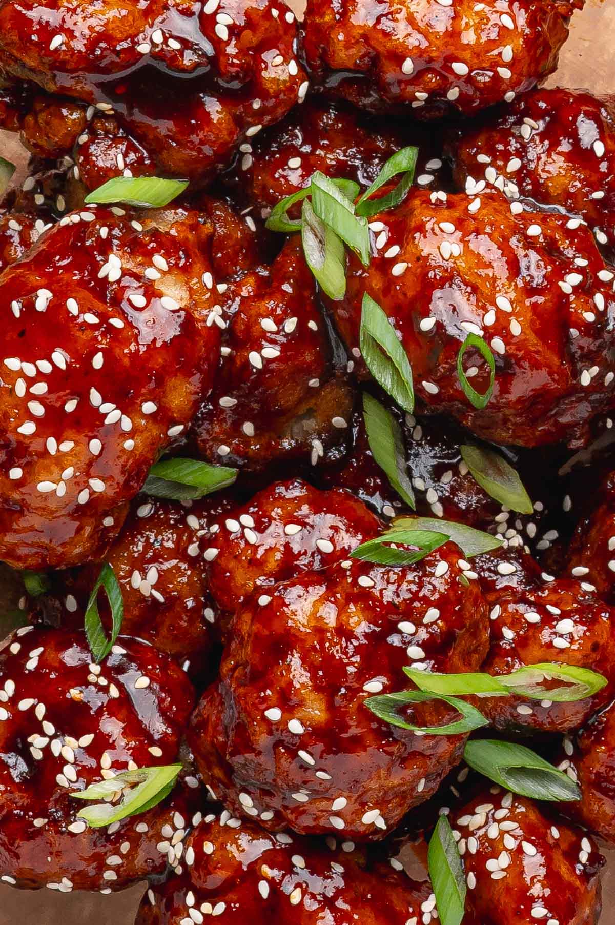 Close up photo of korean fried cauliflower with garnishes of green onion and sesame seeds.
