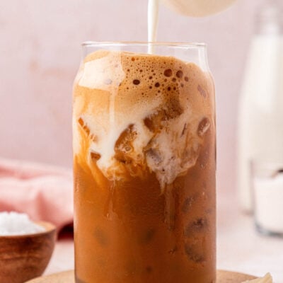 Cream being poured into a glass filled with iced coffee.