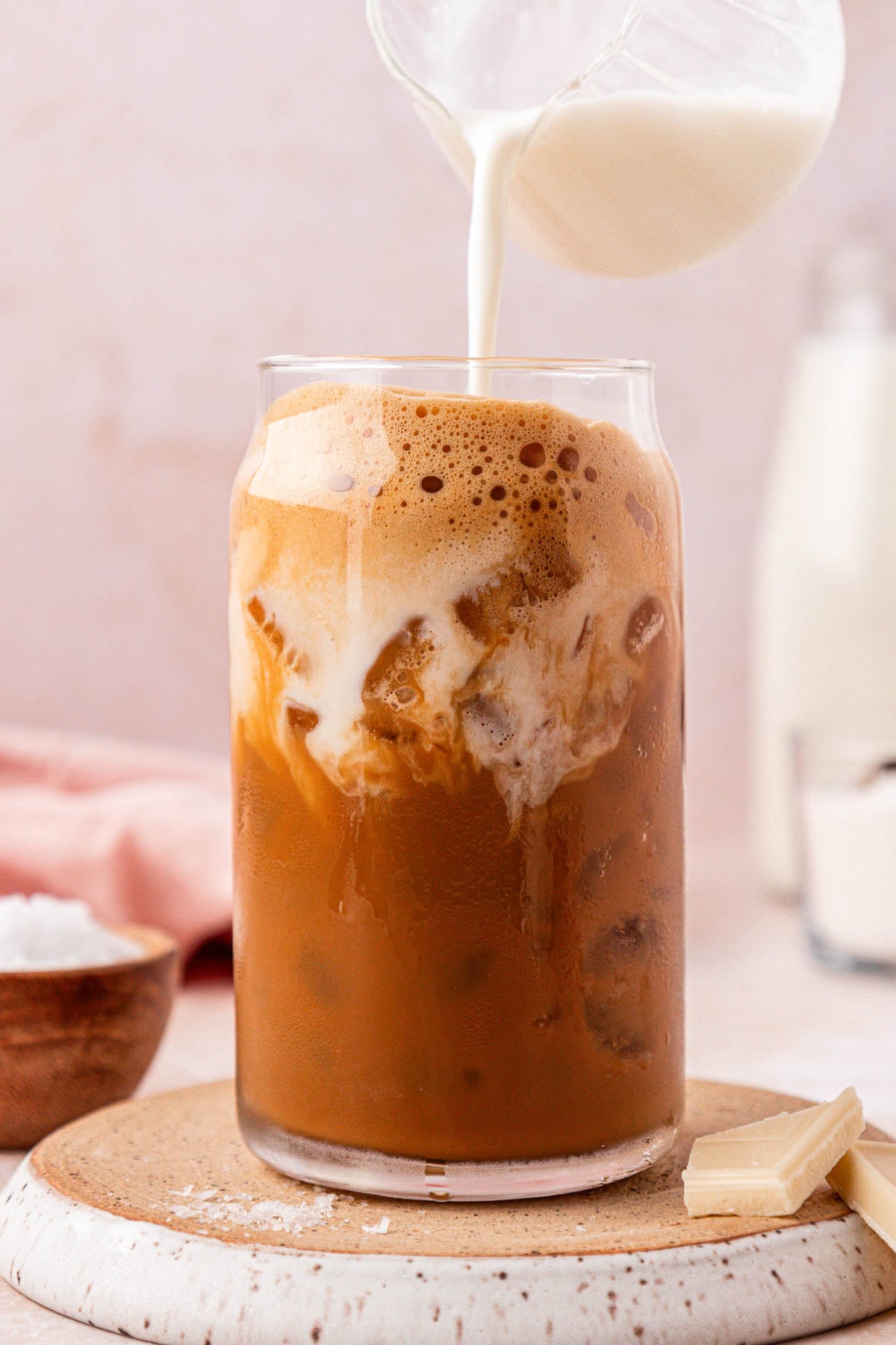 Cream being poured into a glass filled with iced coffee.